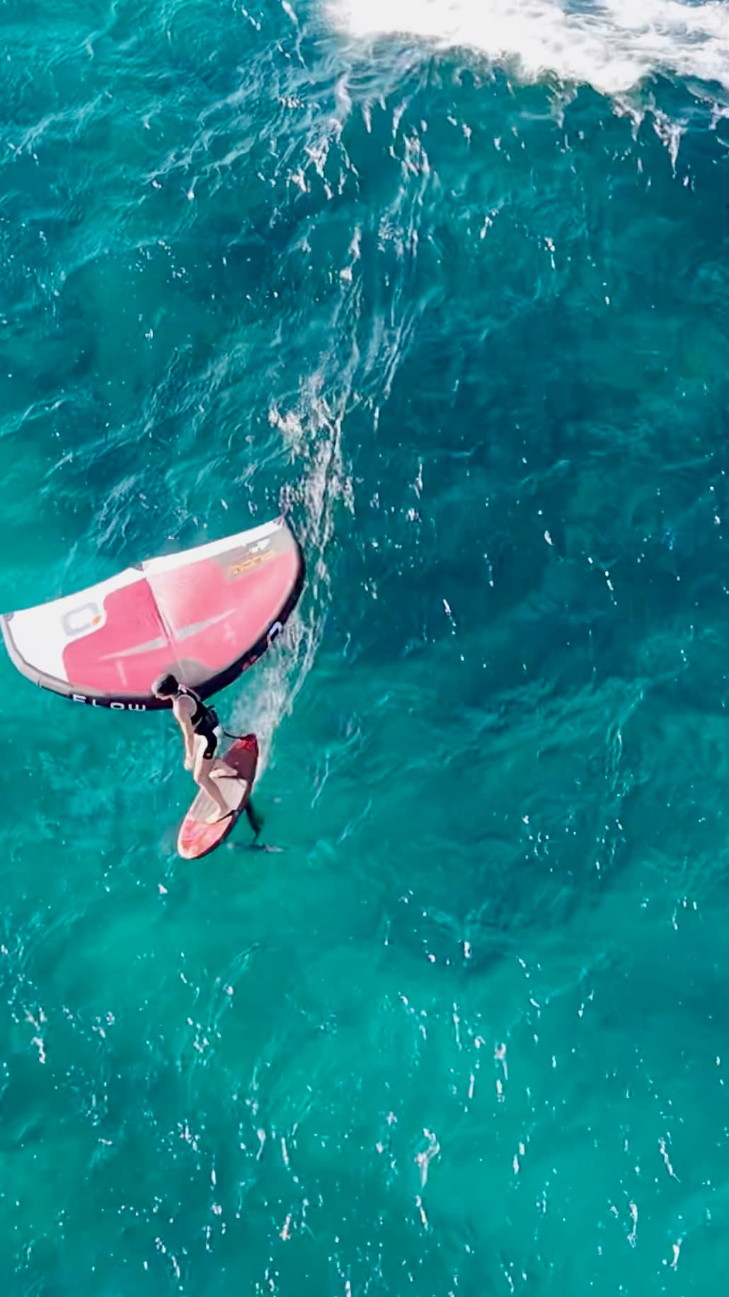 Aerial view of wing foiling over turquoise water with a pink handheld wing