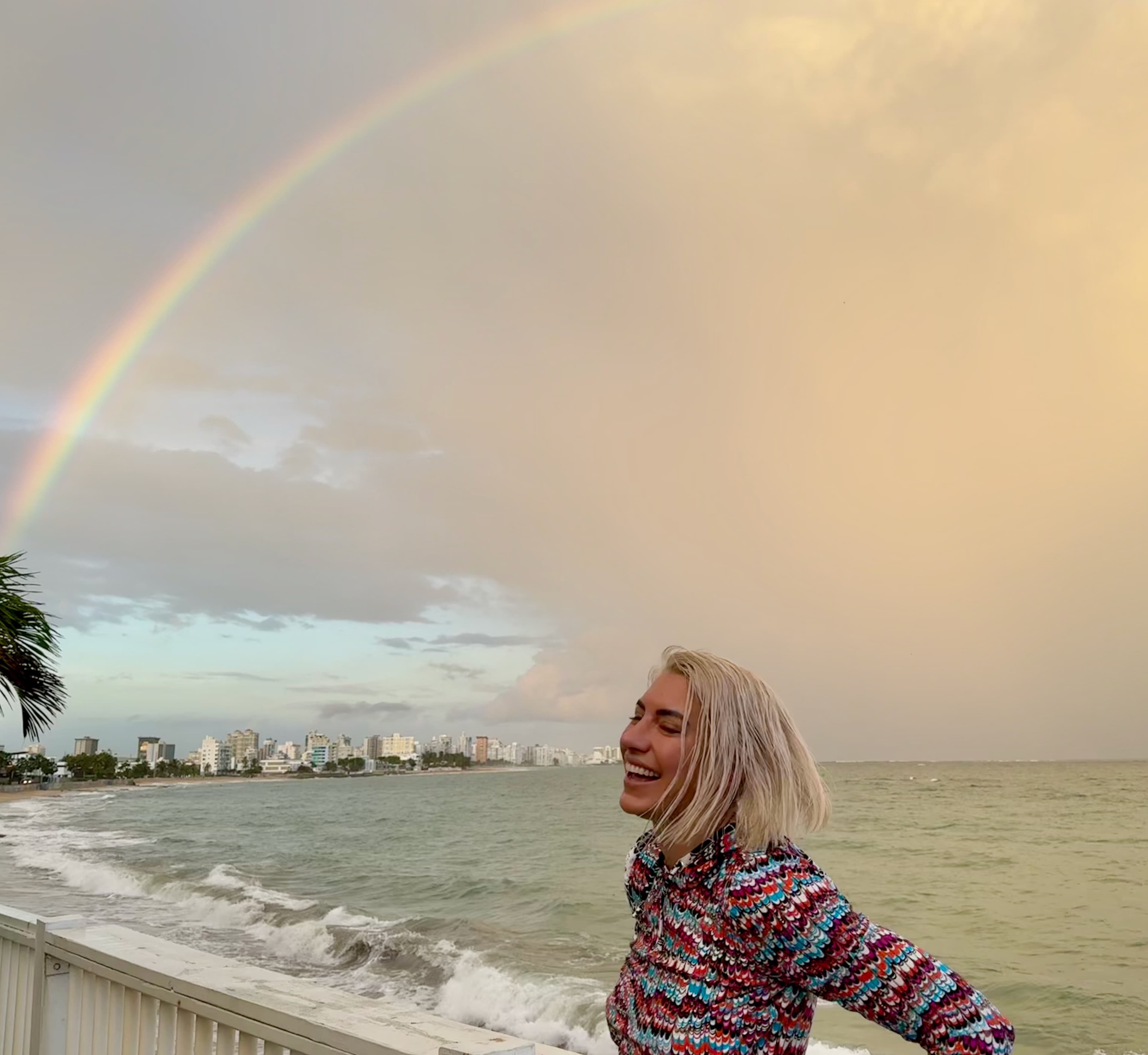 Wren smiling beside the ocean under a rainbow